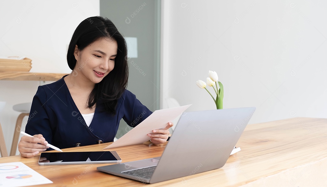 Jovem empresária asiática trabalha em tablet com laptop no escritório.