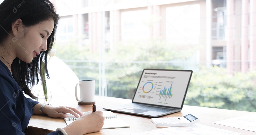 Bela empresária asiática analisa gráficos usando calculadora de laptop no escritório.