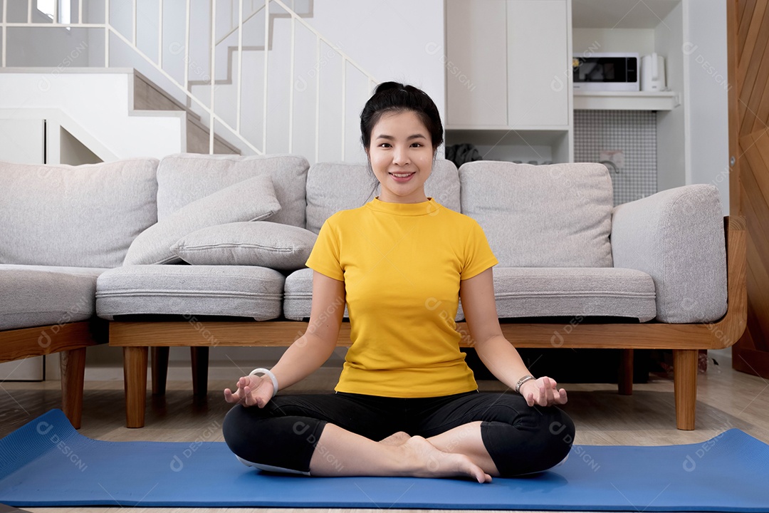 Jovem praticando meditação sentada no colchonete em casa