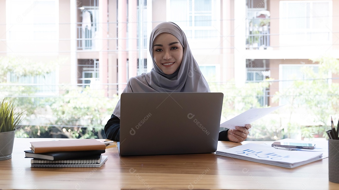 Mulher muçulmana asiática hijab usando laptop no trabalho sorrindo