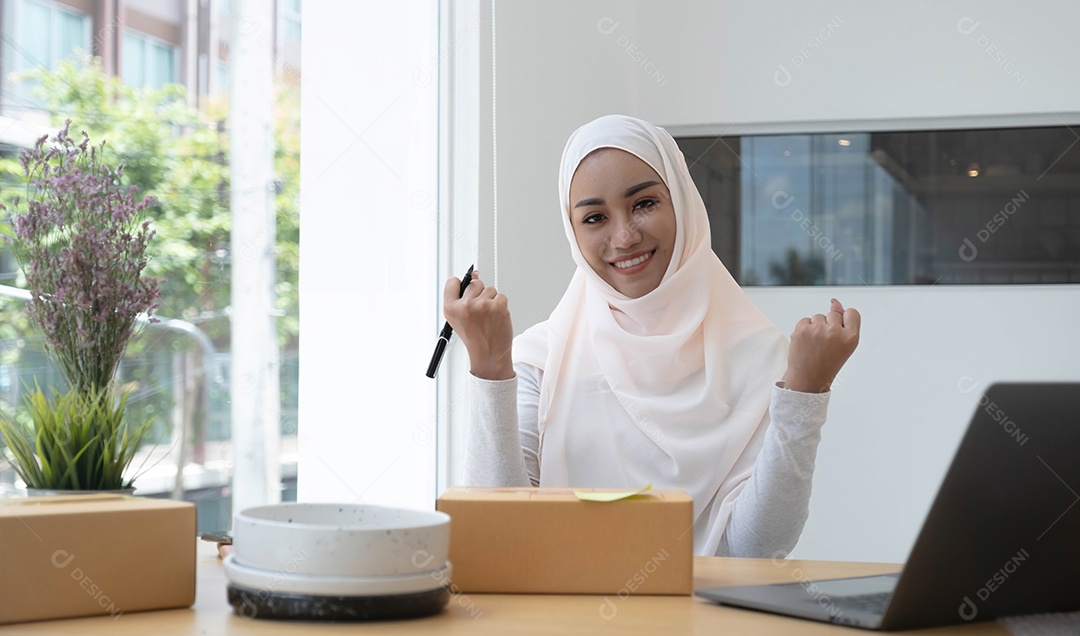 Mulher muçulmana sorridente usando um hijab rosa claro sentado em uma cadeira de escritório.