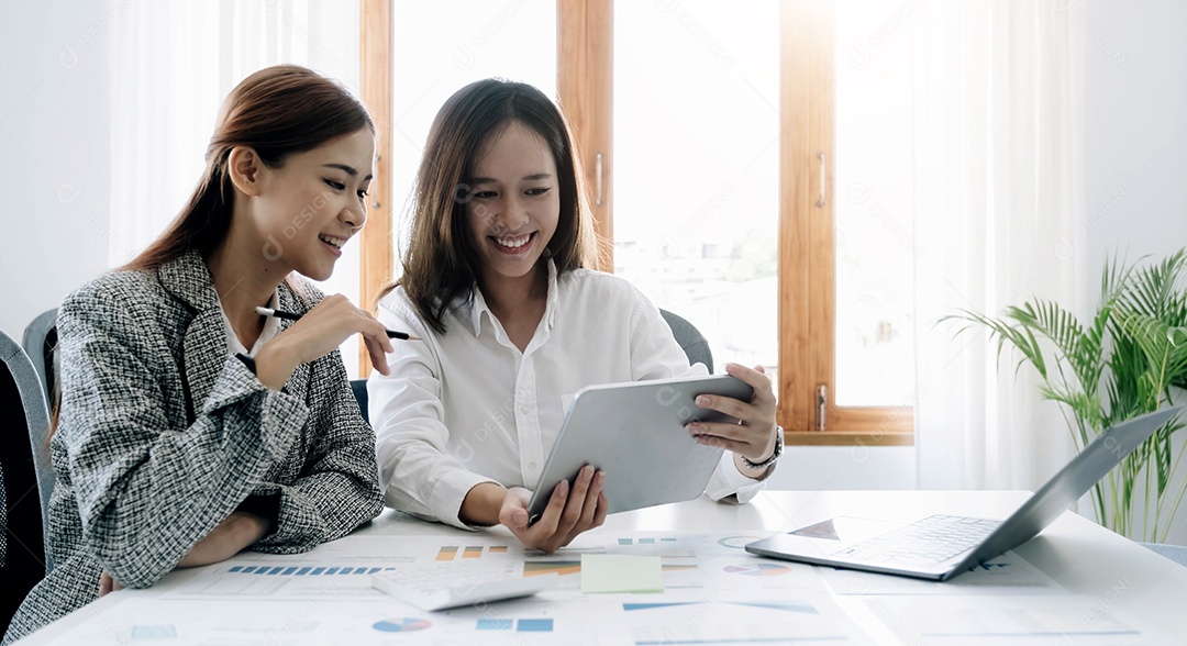 Duas belas jovens empresárias asiáticas trabalhando juntas usando tablet digital no escritório.