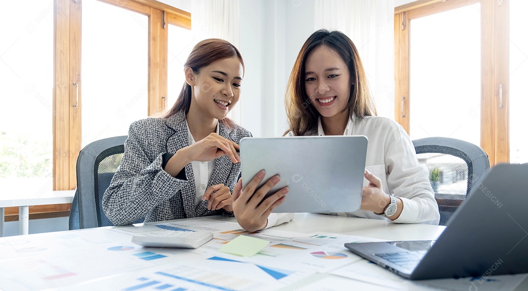 Duas belas jovens empresárias asiáticas trabalhando juntas usando tablet digital no escritório.