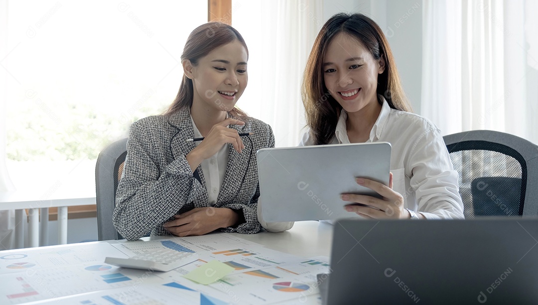 Duas belas jovens empresárias asiáticas trabalhando juntas usando tablet digital no escritório.