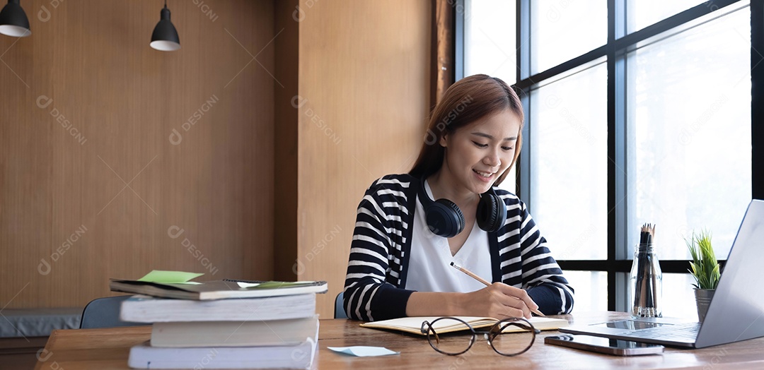 Aluna adolescente asiática sorridente estuda na biblioteca com livros e laptop fazendo pesquisas on-line para cursos
