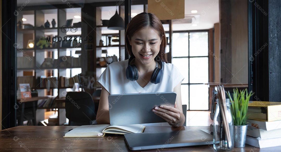 Mulher jovem asiática sorridente usando fone de ouvido olhando para a tela do laptop, ouvindo e aprendendo cursos on-line.