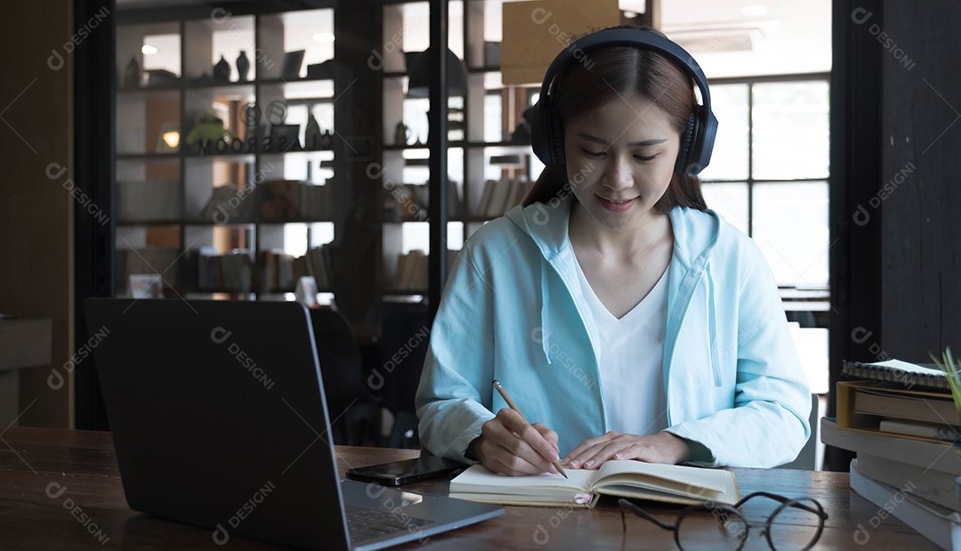 Mulher jovem asiática sorridente usando fone de ouvido olhando para a tela do laptop