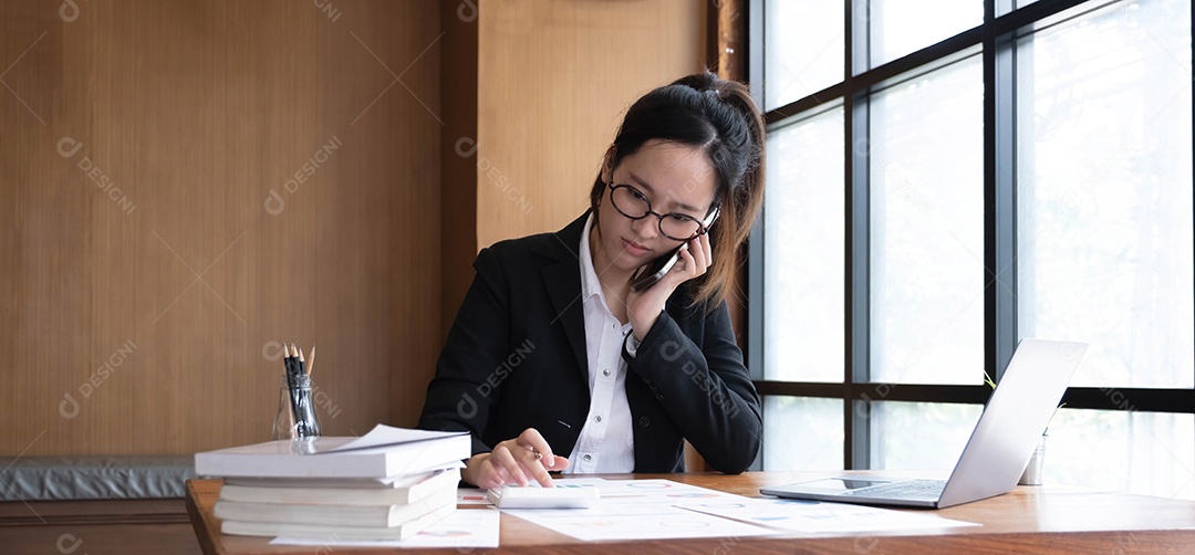 Mulher de negócios asiática séria usando laptop olhando para o computador falando no telefone