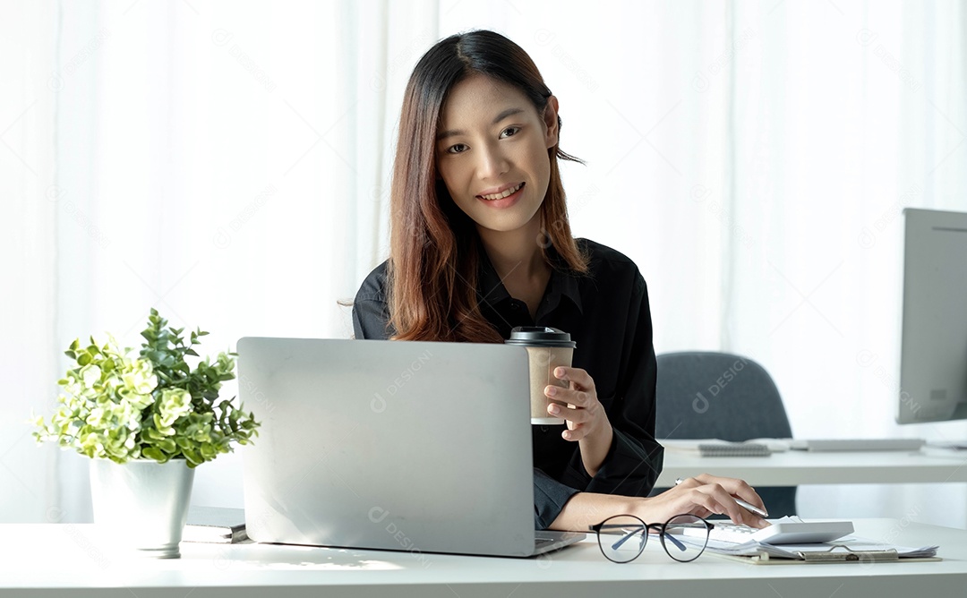 Empresária asiática sorridente segurando uma caneca de café e laptop