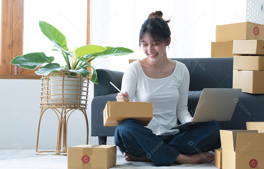 Uma jovem empresária asiática sorridente prepara uma caixa de encomendas