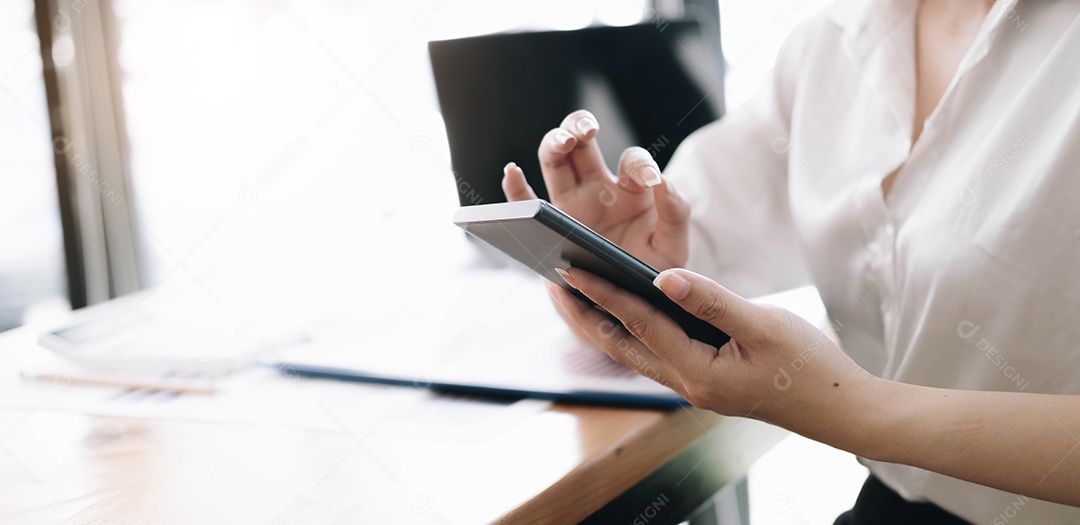 Mão de uma mulher usando smartphone no escritório.