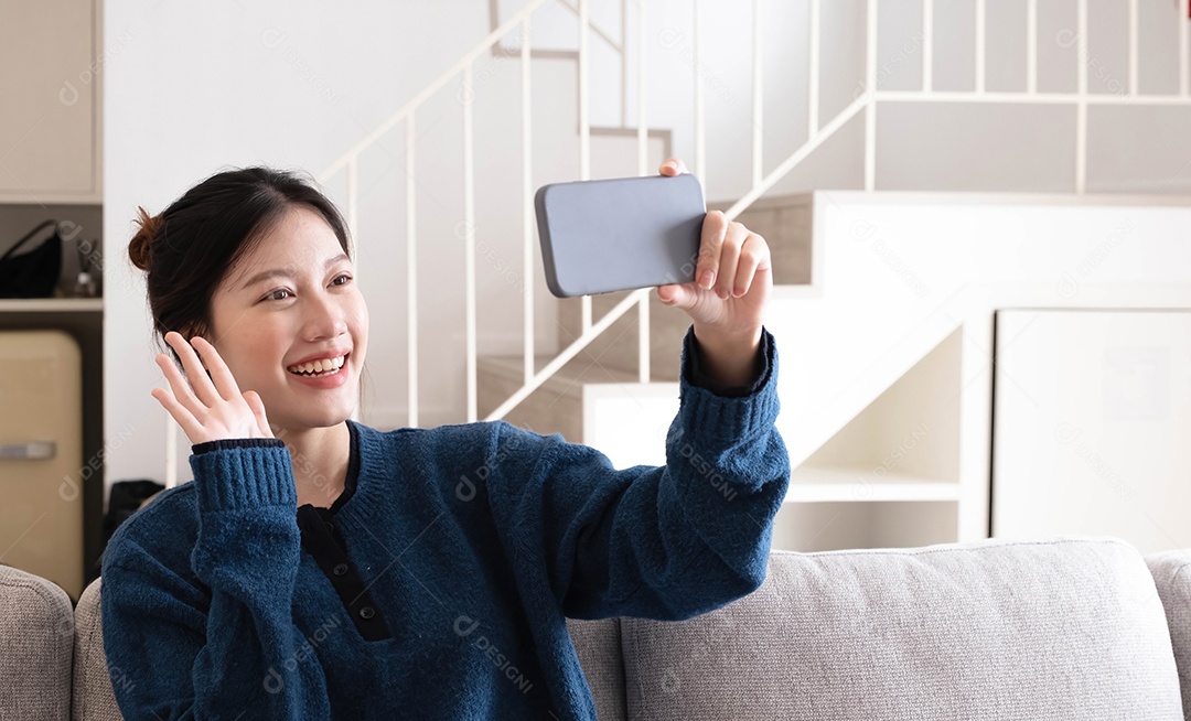 Sorrindo jovem mulher asiática usando telefone celular enquanto está sentado