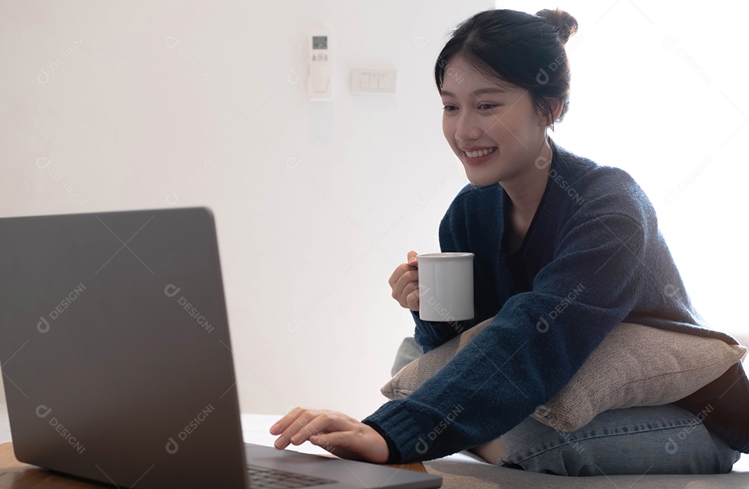 Linda mulher asiática bonita e alegre sorridente que relaxa bebendo e usa laptop.