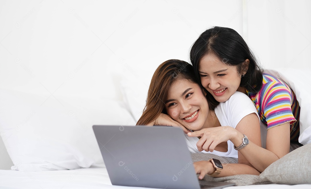 Um casal de mulheres adoráveis ​​ouvindo música e assistindo filme com o laptop na cama