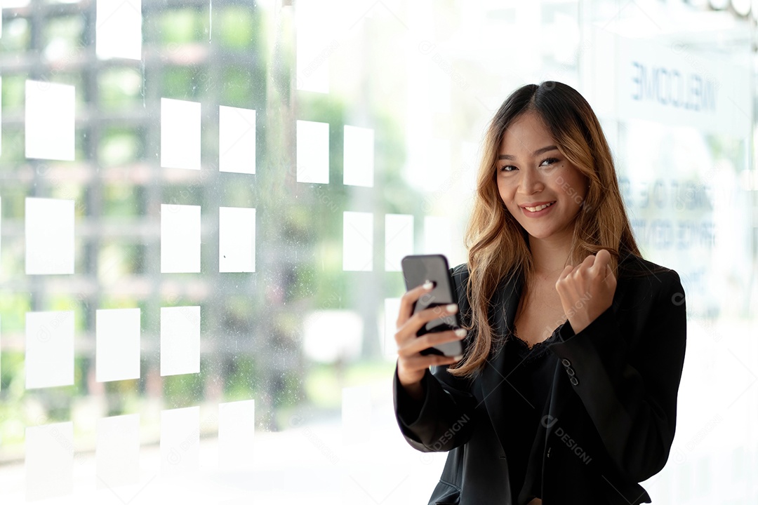 Linda mulher asiática usando smartphone, emocionada e comemorando com boas notícias