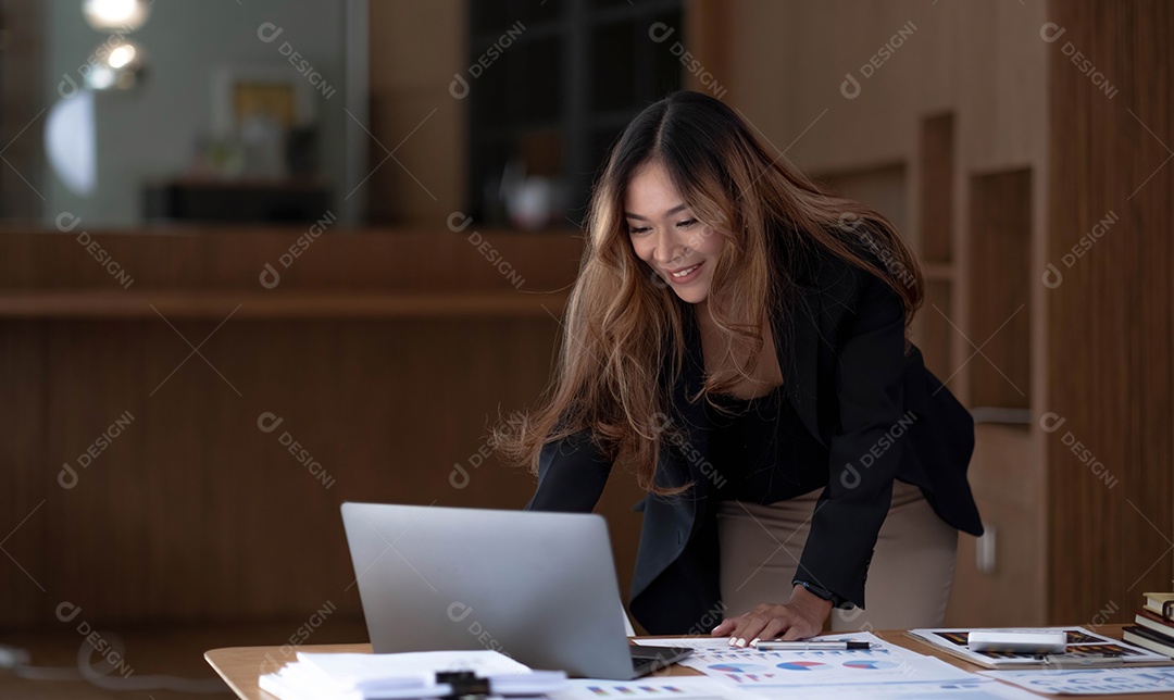 Bela empresária asiática analisa gráficos usando calculadora e laptop no escritório.