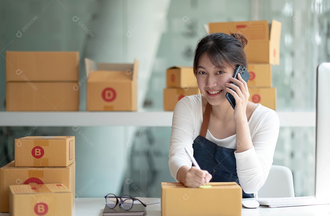 Mulher jovem e pequena empresária asiática segura caneta e caixas de encomendas