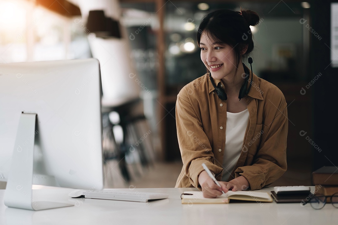 Mulher asiática usando fones de ouvido usando laptop e fazendo anotações