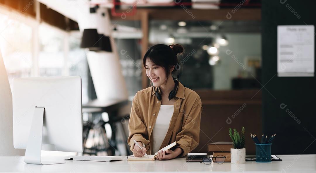 Mulher asiática usando fones de ouvido usando laptop e fazendo anotações