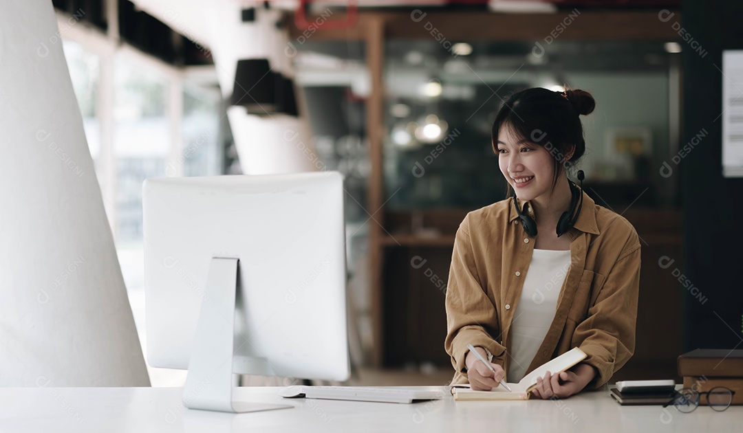 Mulher asiática usando fones de ouvido usando laptop e fazendo anotações