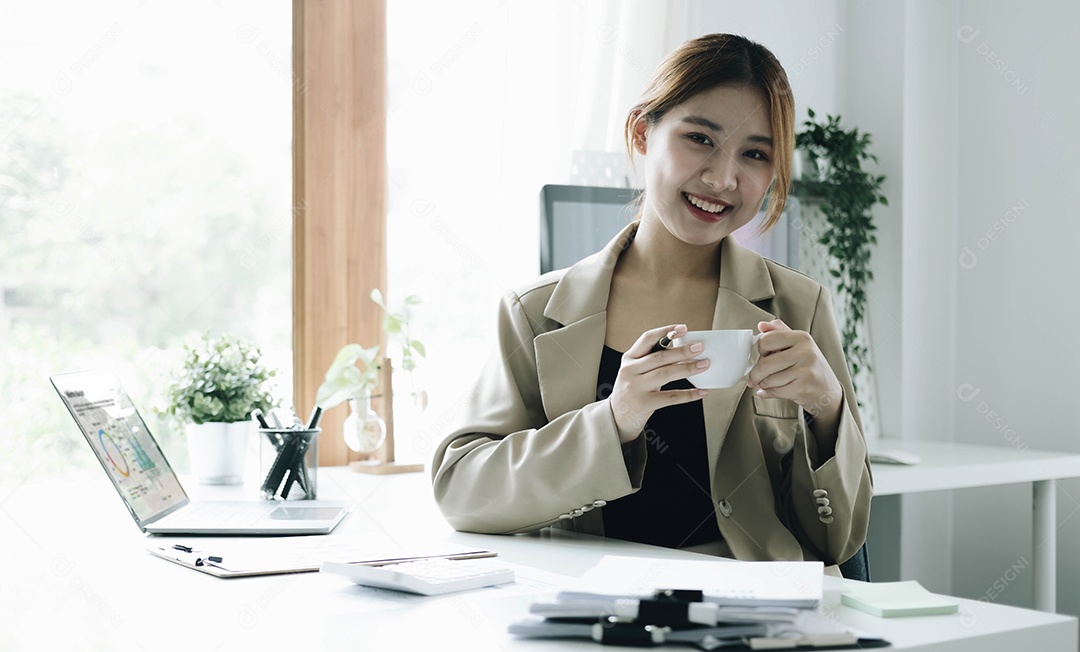 Empresária asiática sorridente segurando uma caneca de café e laptop