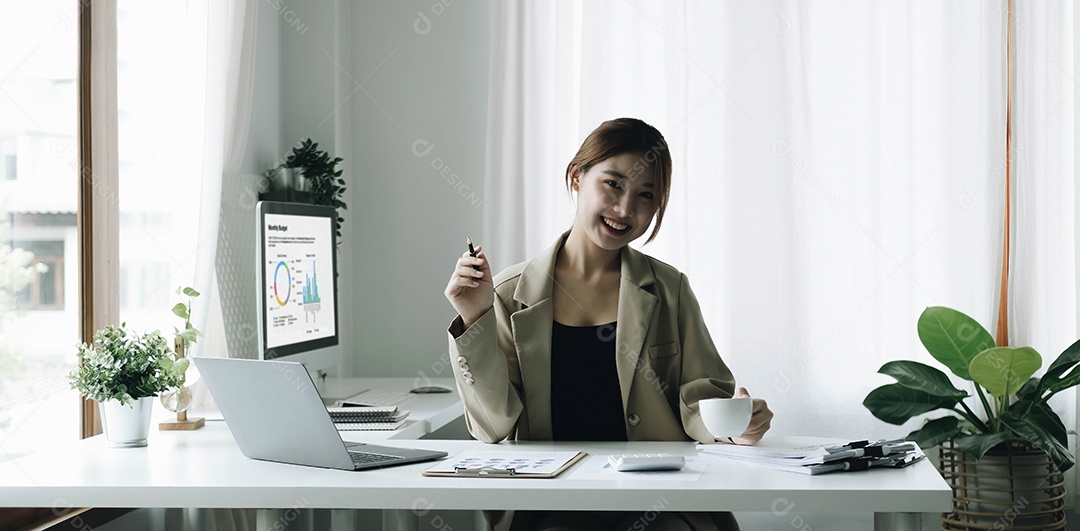 Empresária asiática sorridente segurando uma caneca de café e laptop