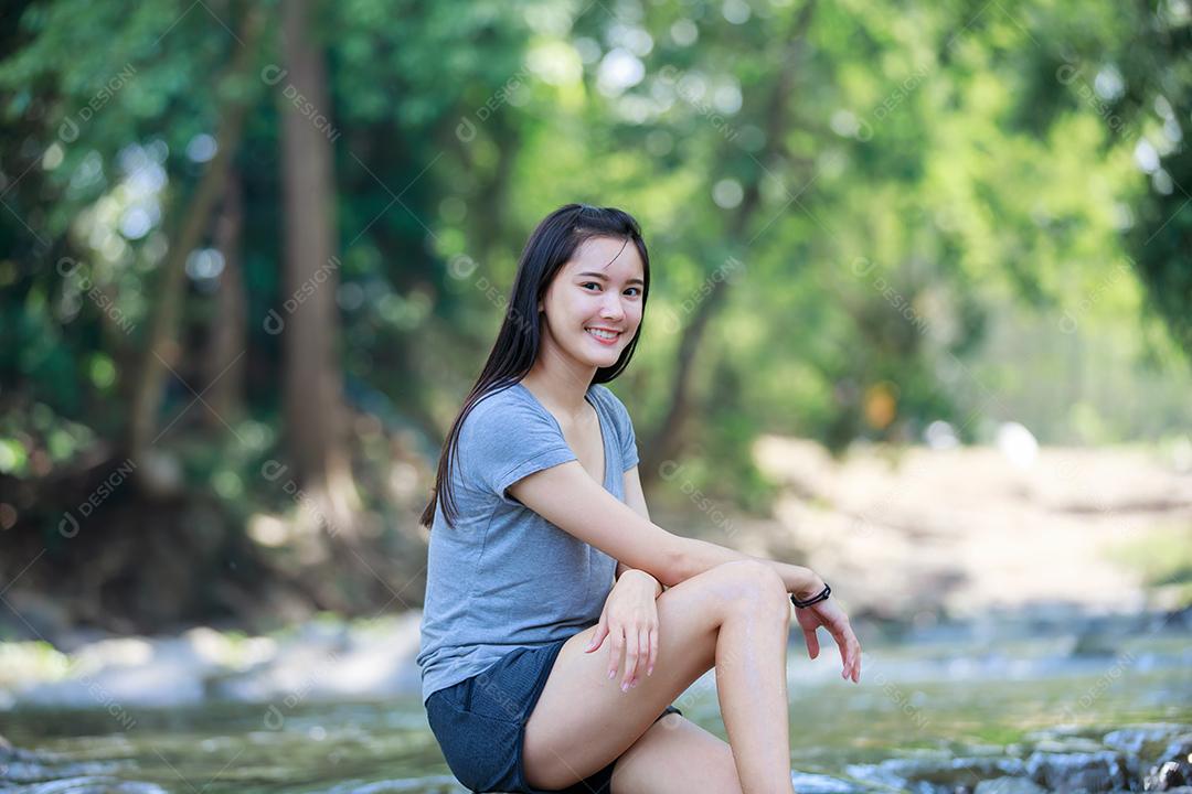 A garota está sentada em uma cachoeira e sorrindo feliz, foco suave e borrão
