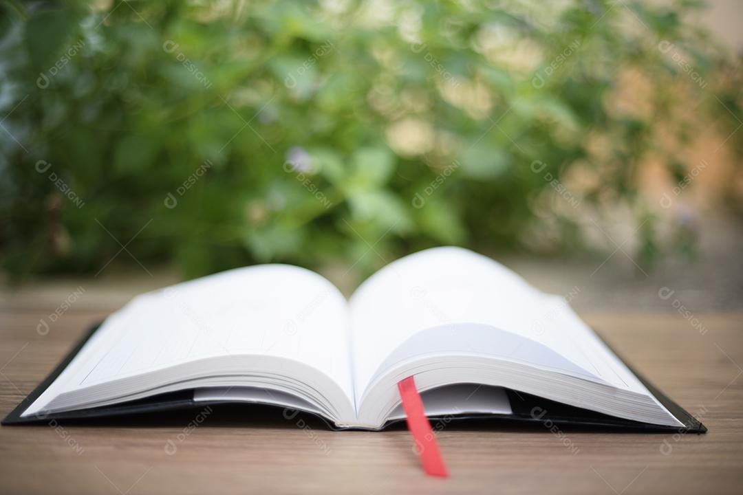 Um livro aberto na mesa de madeira no jardim de casa com fundo de natureza bokeh