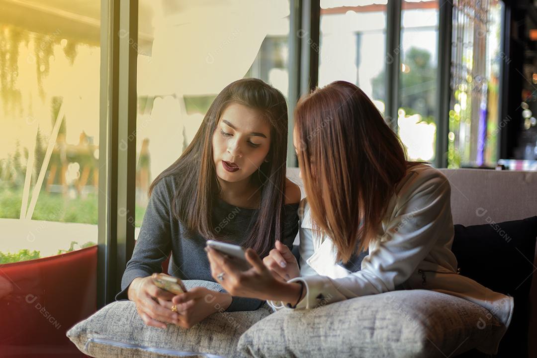 Jovem olhando para o telefone de sua amiga e se sentindo excitante e sorrindo enquanto está sentado na sala de estar em casa