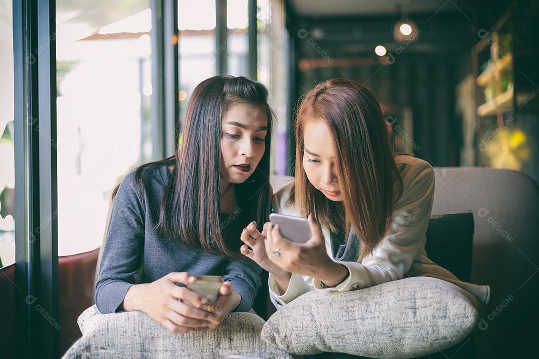 Jovem olhando para o telefone de sua amiga e se sentindo excitante e sorrindo enquanto está sentado na sala de estar em casa