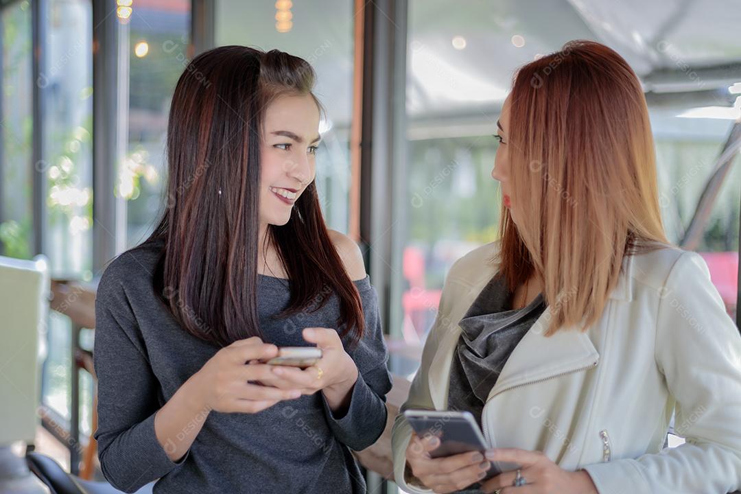 Jovem olhando para o telefone de sua amiga e se sentindo excitante e sorrindo enquanto está sentado na sala de estar no escritório