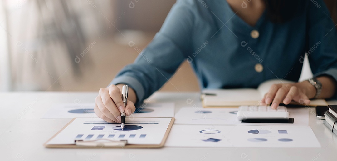 Mulher apontando para papelada e usando a calculadora.