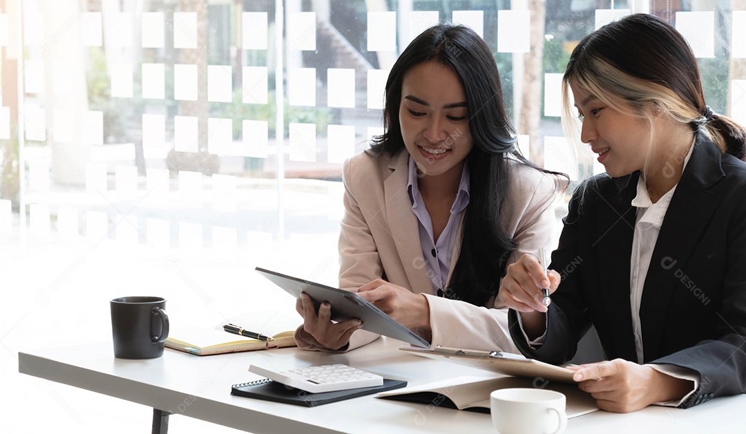 Duas belas jovens empresárias asiáticas trabalhando juntas usando tablet