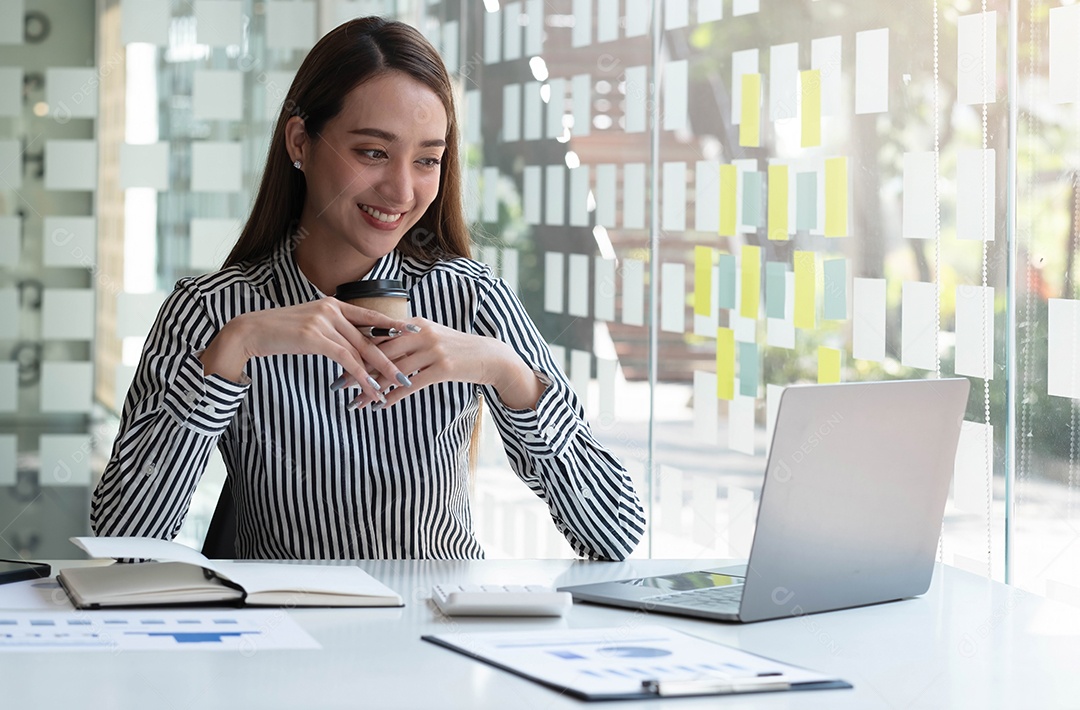 Empresária asiática sorridente segurando uma caneca de café e laptop