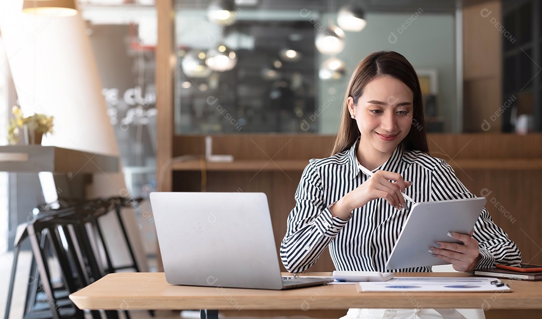 Feliz jovem empresária asiática sentada em seu local de trabalho