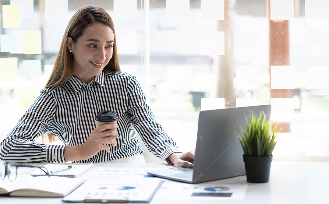 Bela jovem asiática sentada na cafeteria usando o laptop.