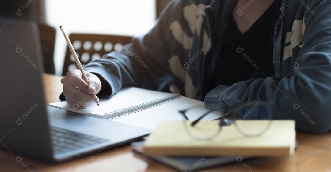 Mulher usando laptop e anotando alguns dados no bloco de notas