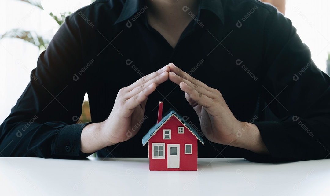 Mão de uma pessoa protegendo a casa em miniatura na mesa