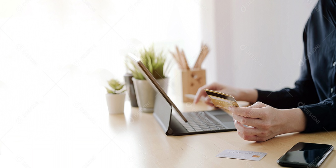 Mão de uma mulher segurando o cartão de crédito e usando o computador portátil