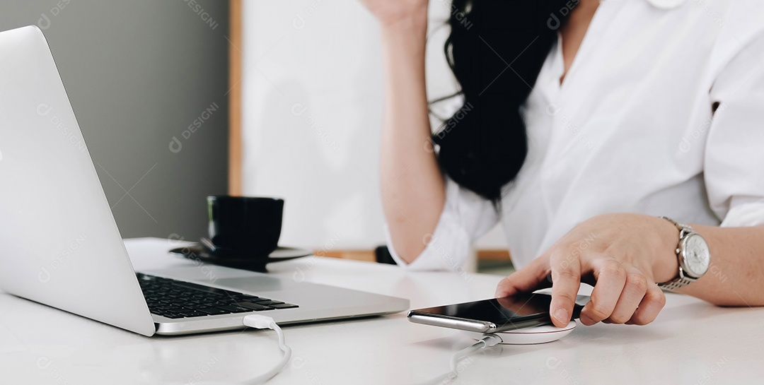 Mulher trabalhando na mesa enquanto seu celular carrega com dispositivo sem fio