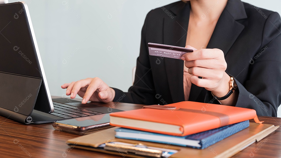 A mão de uma mulher segura um cartão de crédito e usa um laptop