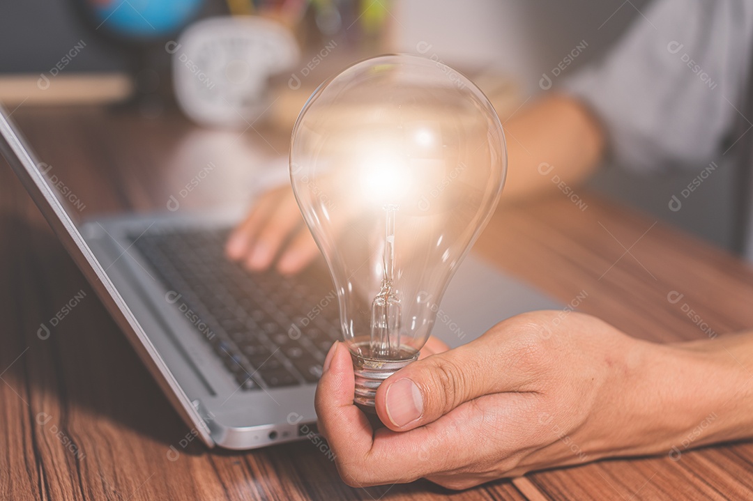 Homem segurando um símbolo de engrenagem de lâmpada enquanto usa um computador
