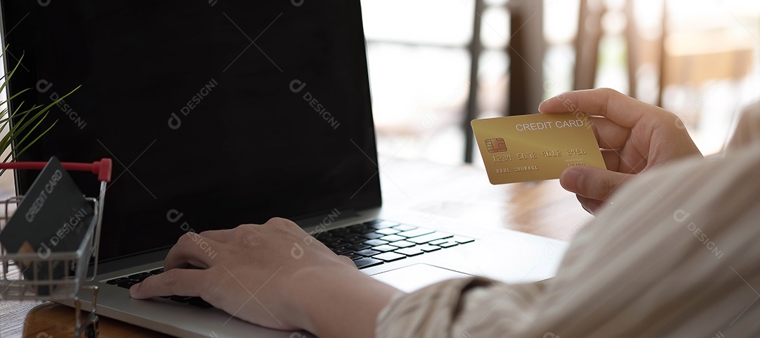 Mão de homem segurando cartão de crédito e usando laptop em casa