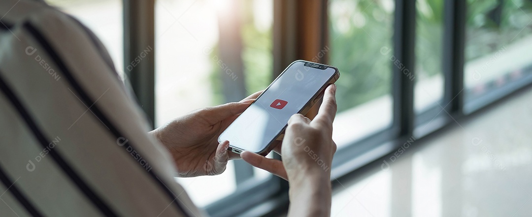 Mulher segurando o iPhone xs com o serviço de vídeo YouTube na tela.