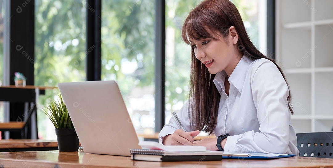 Jovem empresária asiática sentada e feliz trabalhando com laptop