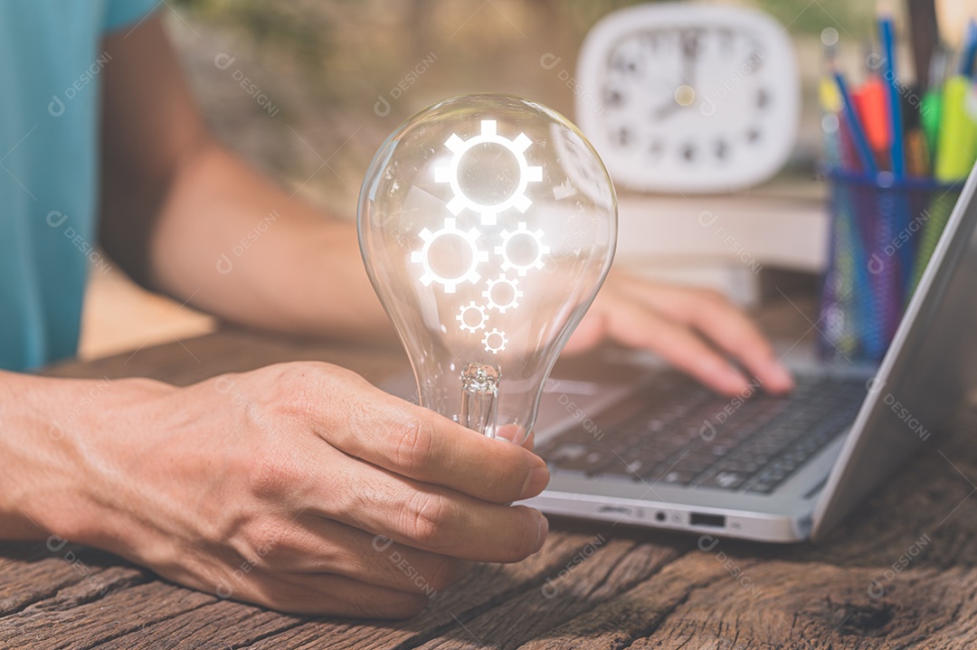 Homem segurando um símbolo de engrenagem de lâmpada enquanto usa um computador