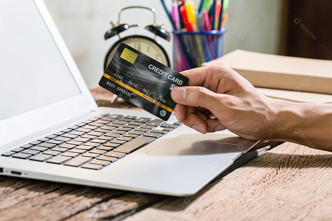 Pessoas usam cartões de crédito para fazer compras online por meio de notebooks.
