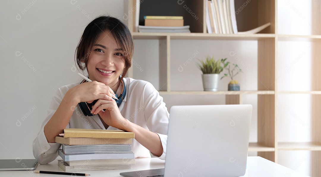 Mulher asiática sorridente trabalhando na mesa com livros e laptop