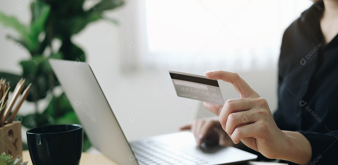 Mãos segurando um cartão de crédito e usando um laptop.