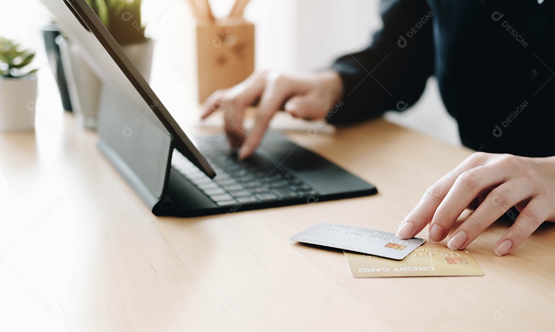 A jovem usa dois cartões de crédito, usando o computador portátil.